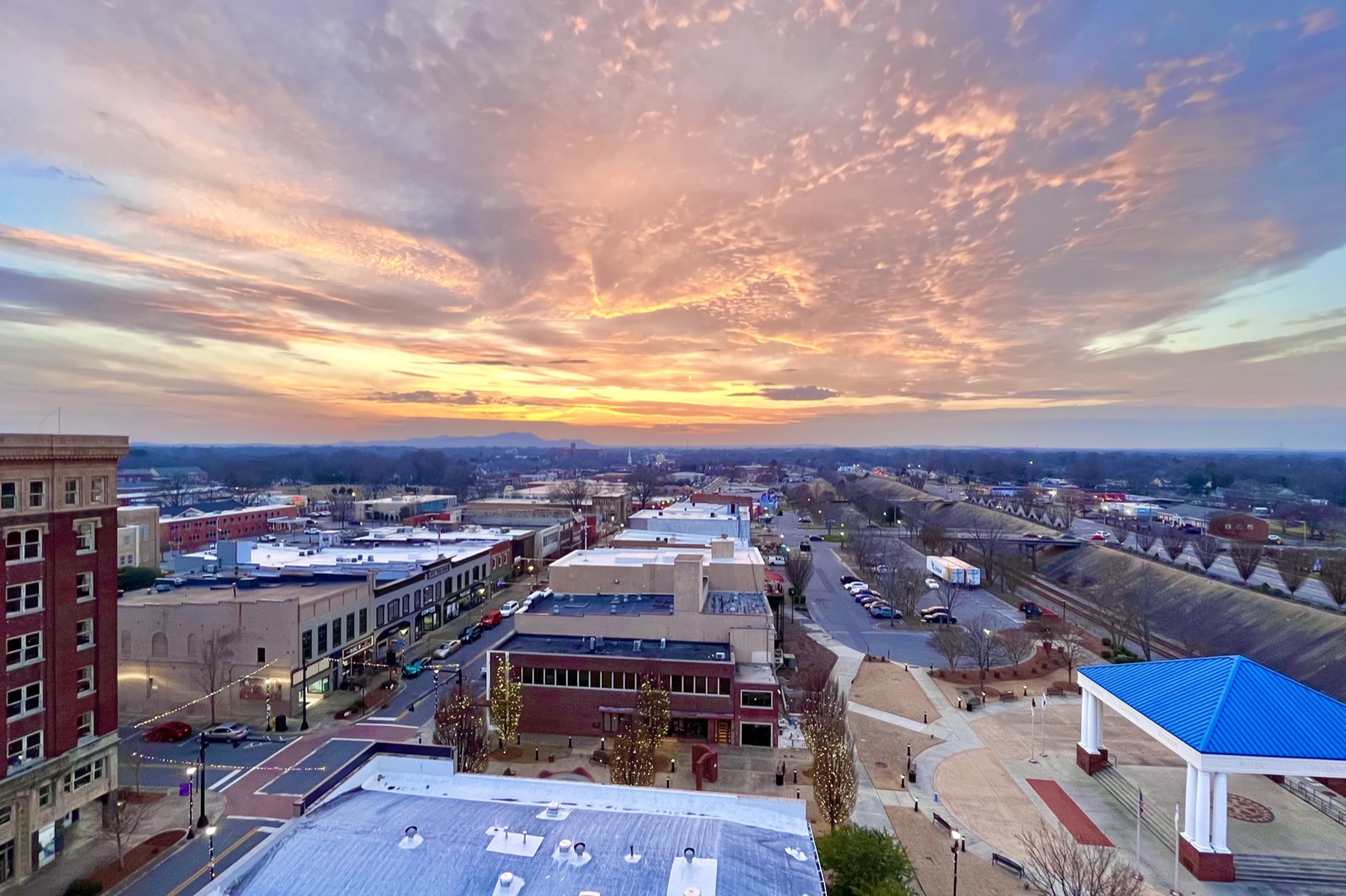 Elevated view of downtown Gastonia, North Carolina at sunset with brick low-rise buildings, streets and a blue-roofed pavilion under pink and orange clouds