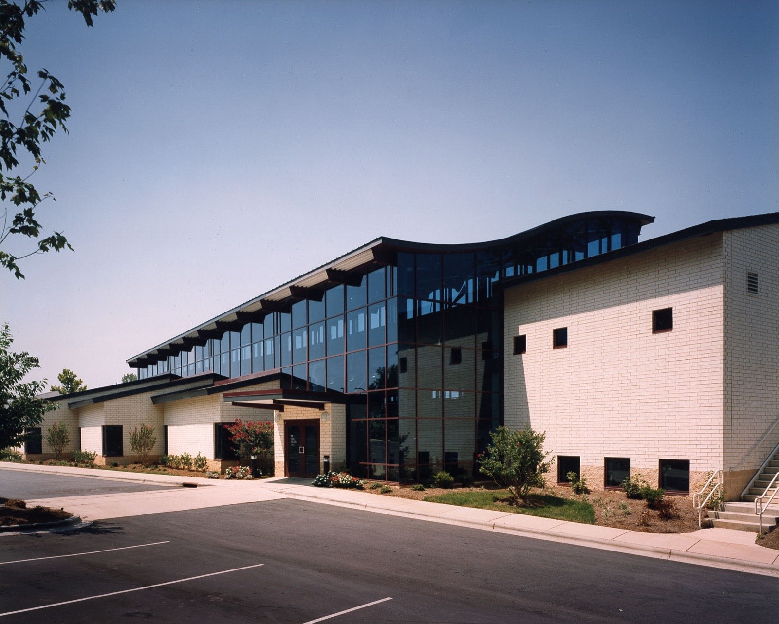 Cream brick and glass exterior of the North County Regional Library in Huntersville, North Carolina, with a curved wave-shaped roofline above a two-story glass entrance