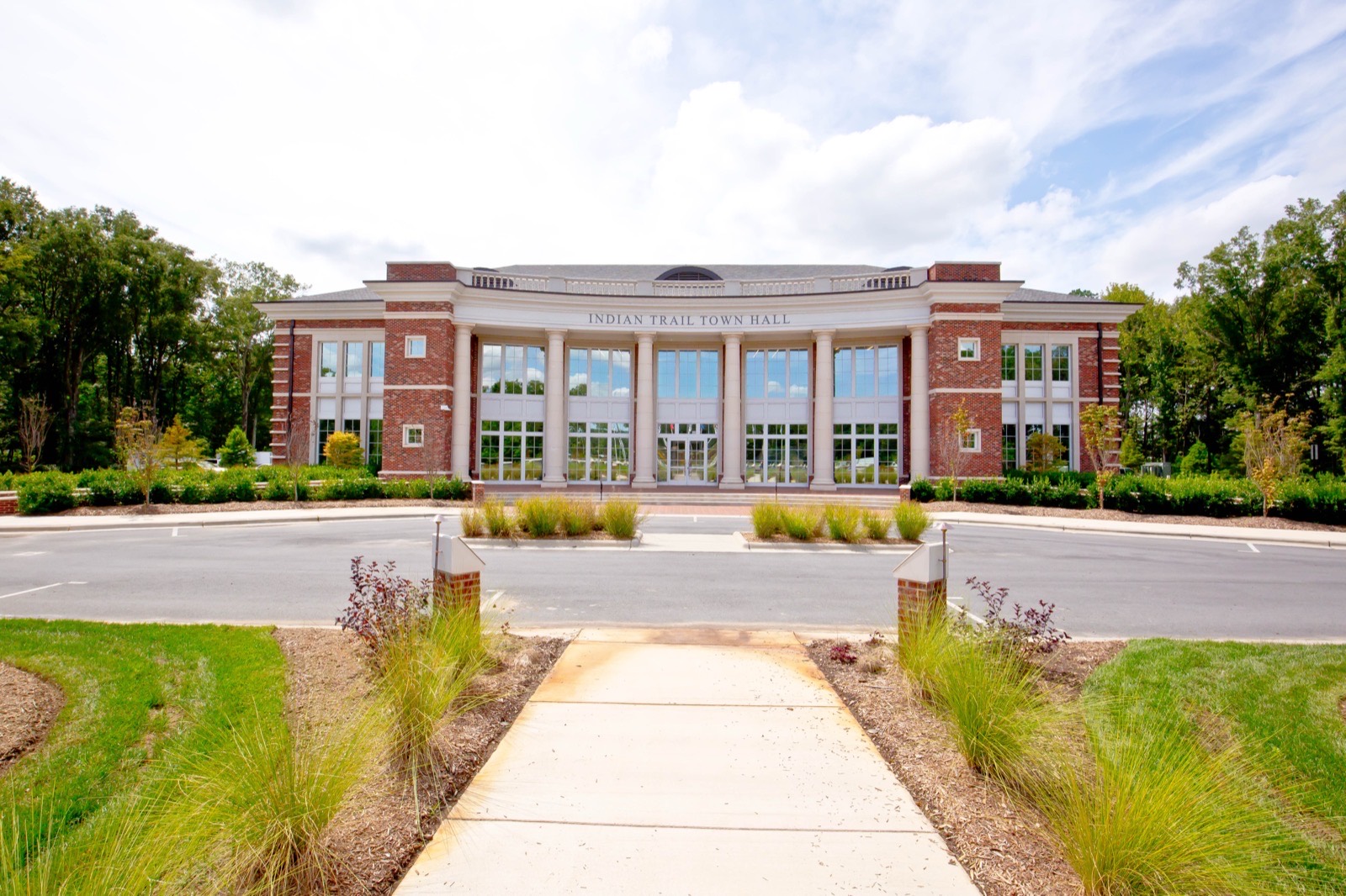 Brick and white-columned Indian Trail Town Hall building with a landscaped walkway and ornamental grasses in Indian Trail, North Carolina